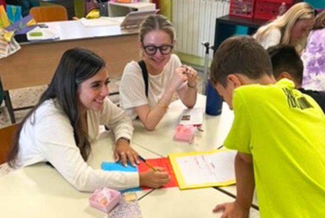 Two students smiling with pupils in classroom with pen in hand.
